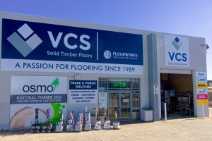 Exterior view of VCS Solid Timber Floors store showcasing a prominent sign featuring the OSMO logo and various flooring equipment outside.